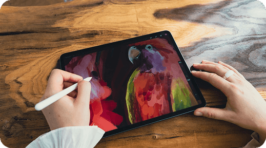 Artist painting a colorful parrot on a tablet with a stylus at a wooden desk
