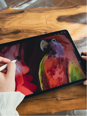 Hand painting a colorful parrot on a tablet with a stylus, on a wooden desk