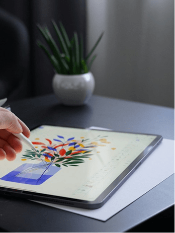 Stylus drawing a vase of bright flowers on a tablet beside a potted plant