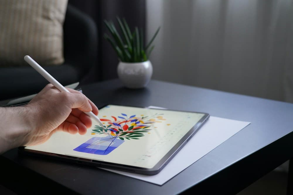 A hand sketching a colourful flower arrangement on a tablet with a stylus.